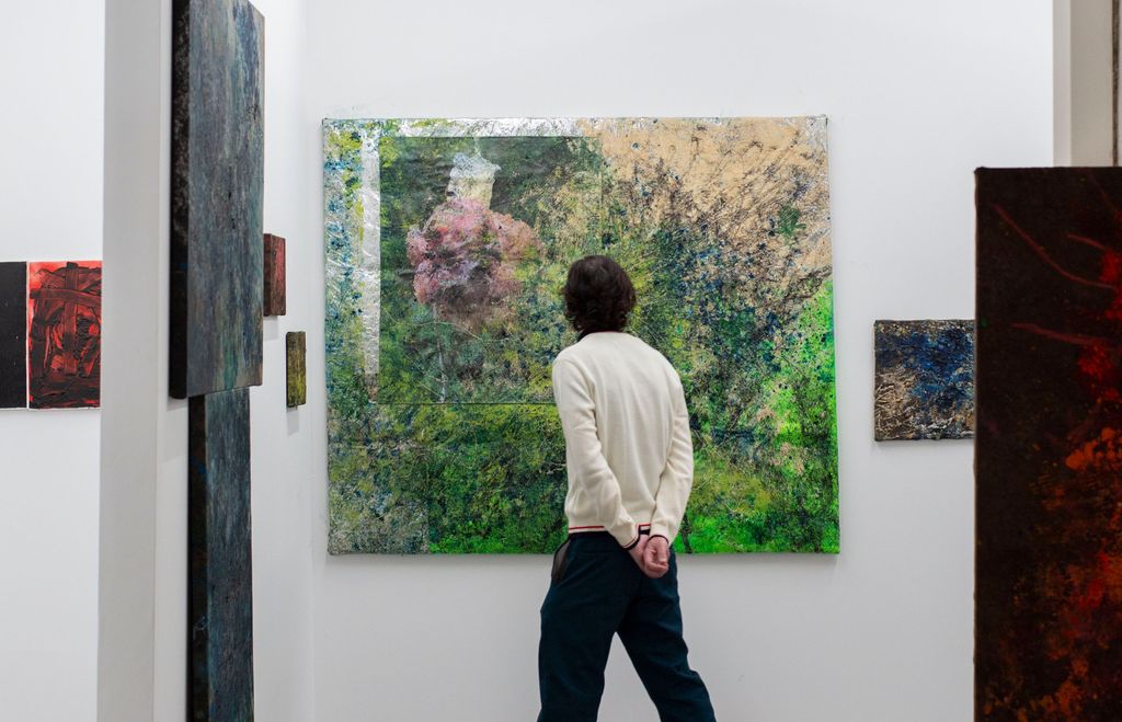 A figure standing looking at a painting at an art fair
